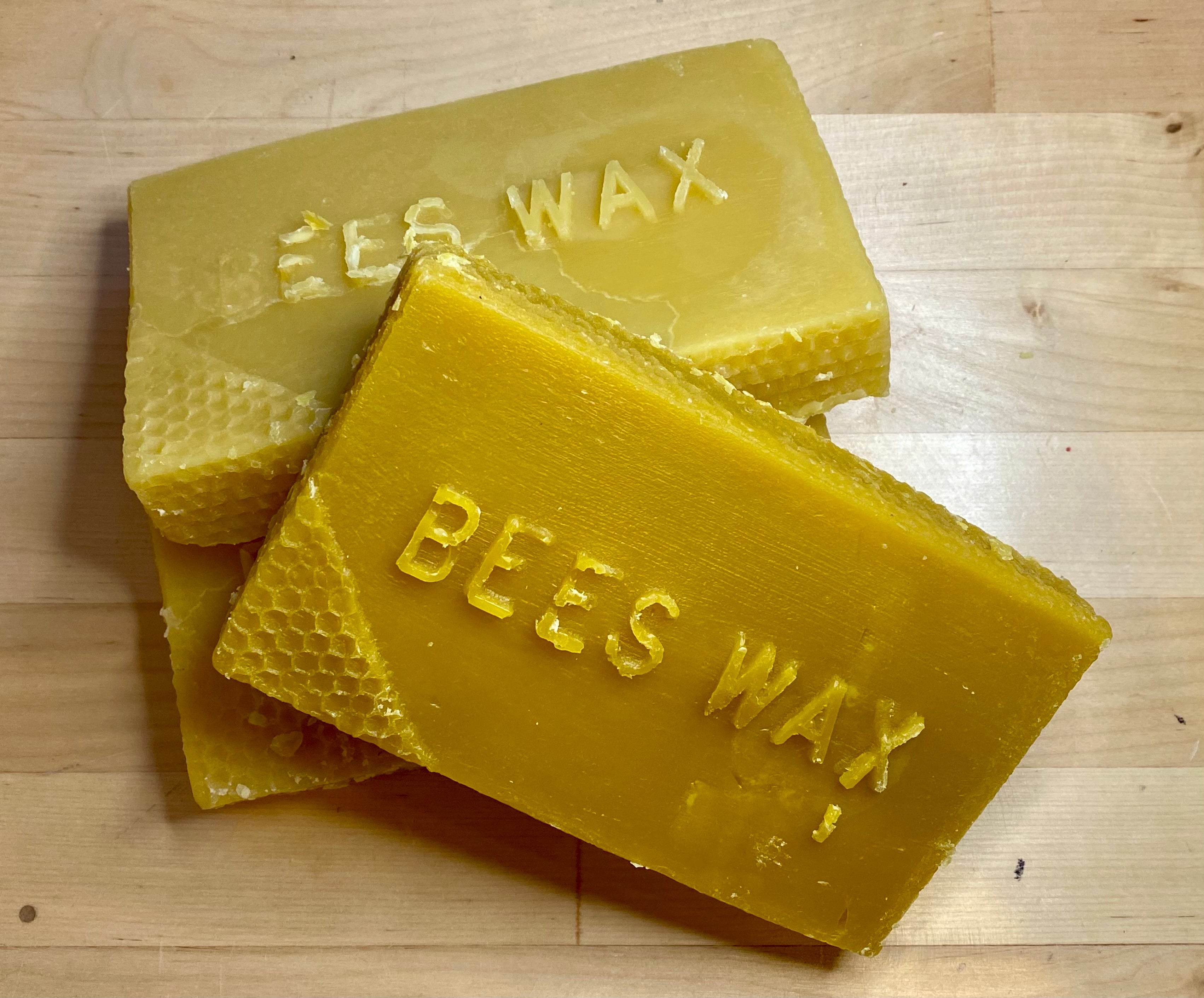 Three rectangular blocks of Shelter Institute's Beeswax Brick, each labeled "BEESWAX," stacked on a wooden surface, serve as a natural lubricant for any woodworking tool.