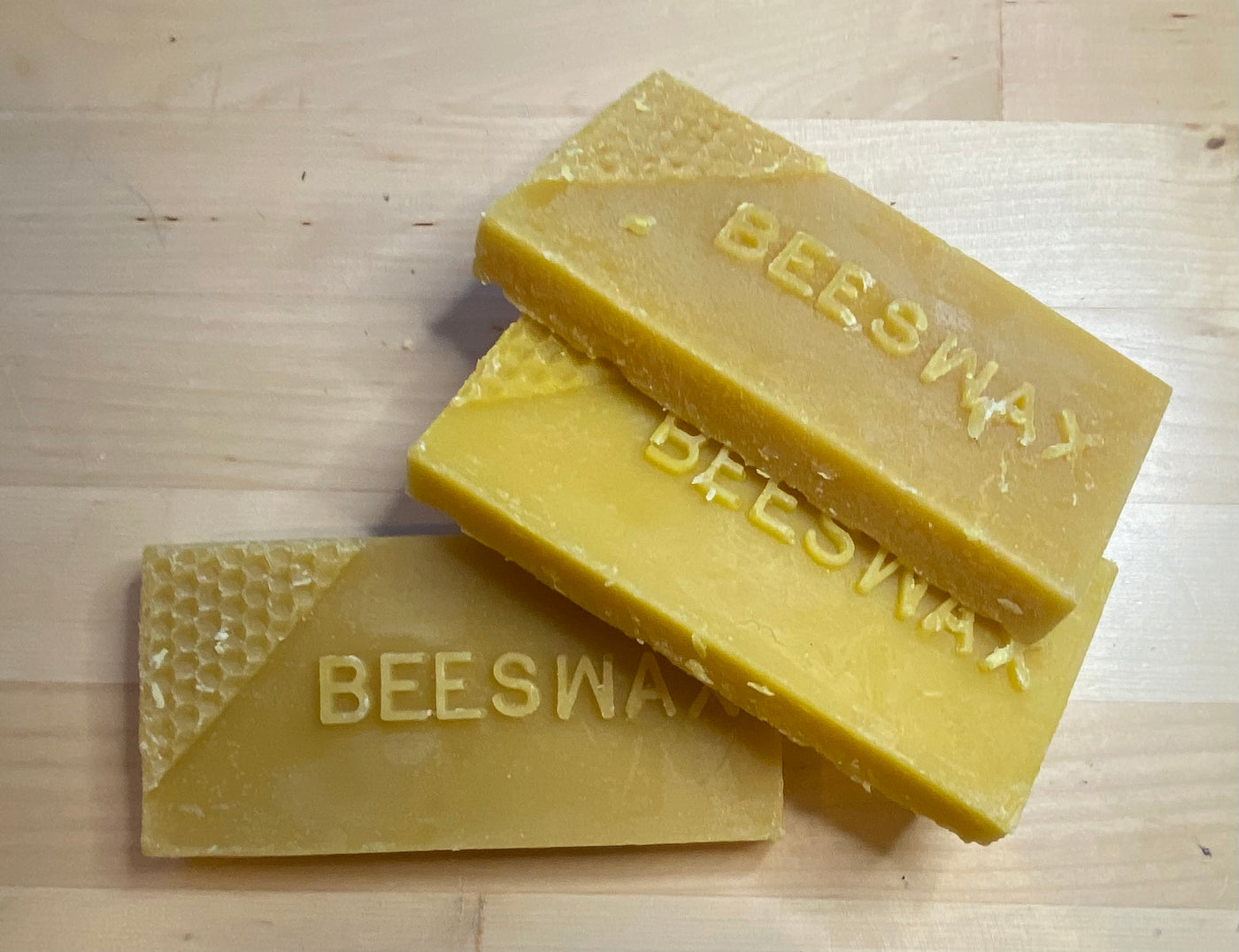 Three Beeswax Bricks from Shelter Institute, each embossed with "BEESWAX," arranged on a wooden surface, serve as a natural lubricant and an essential woodworking tool.