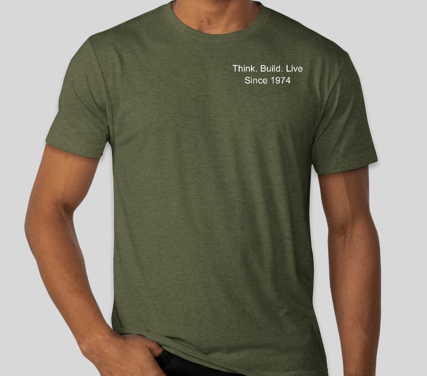 A person is wearing an olive green Custom Ink 50th Anniversary Adult T-Shirt with "Think. Build. Live Since 1974" on the upper left side, celebrating the milestone of building knowledge.