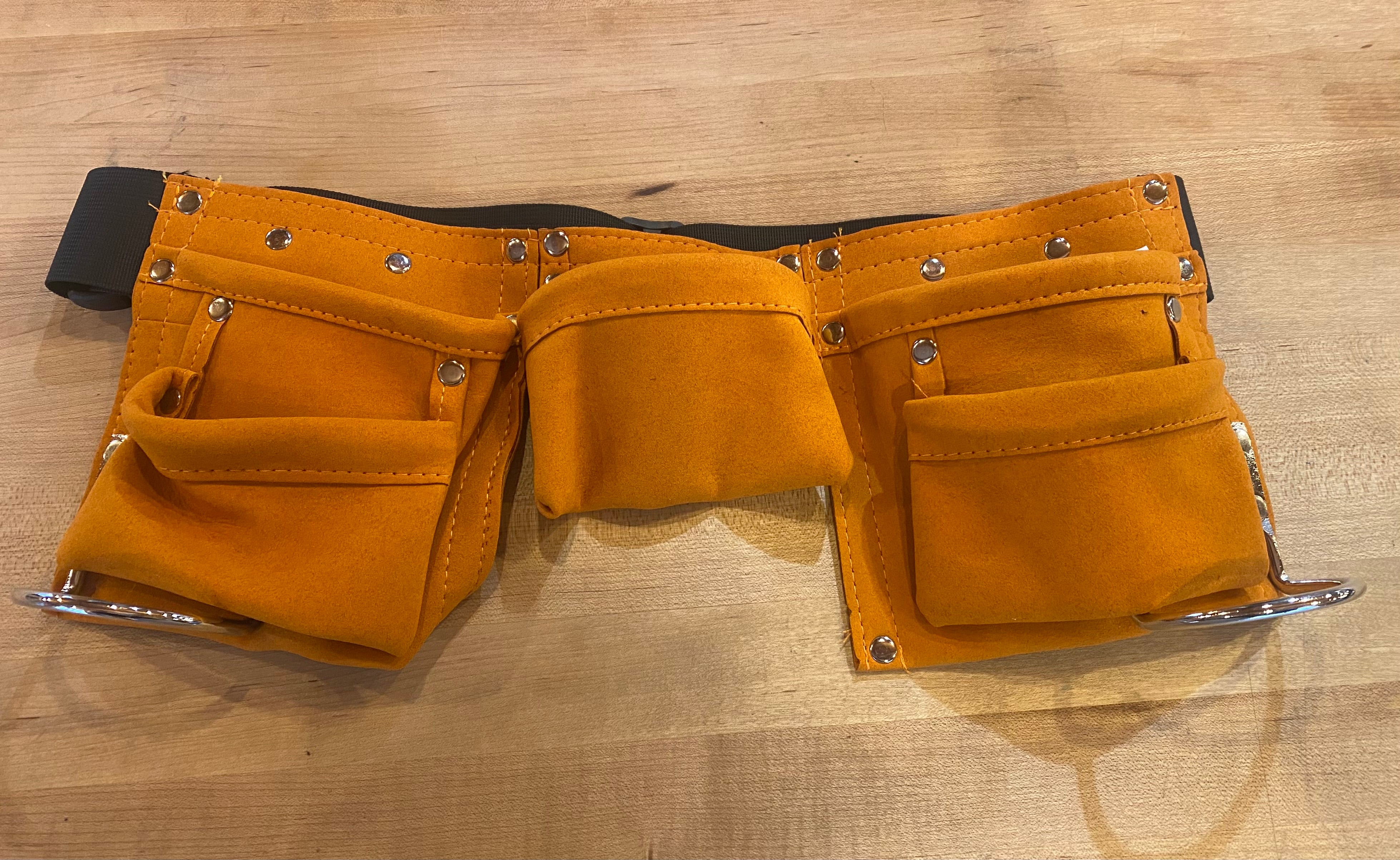 The AMZ Kids Leather Tool Belt, featuring a yellow design with multiple pockets and a black adjustable strap, is shown on a wooden surface.