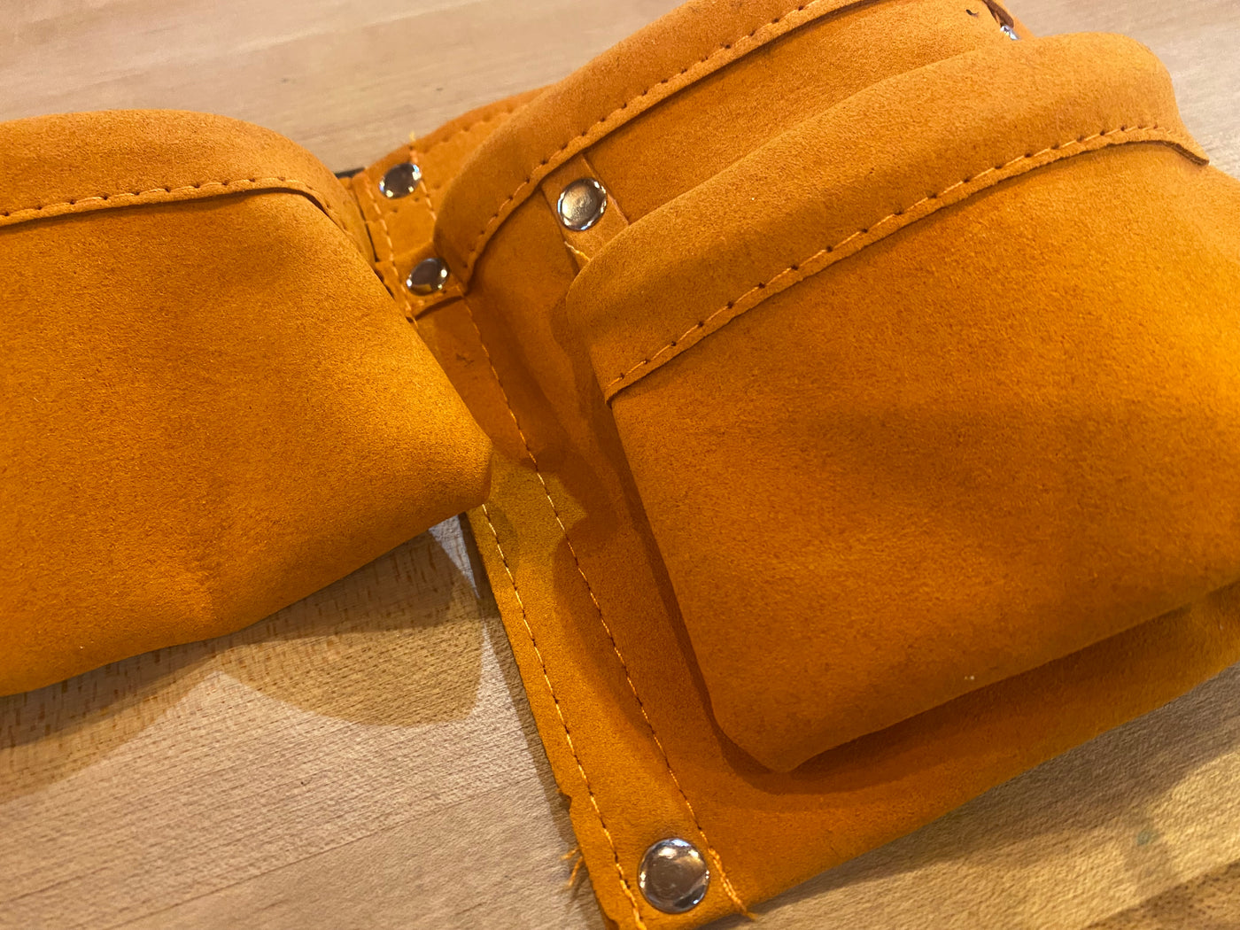 Close-up of an orange AMZ Kids Leather Tool Belt with multiple pockets and metal rivets, resting on a wooden surface.