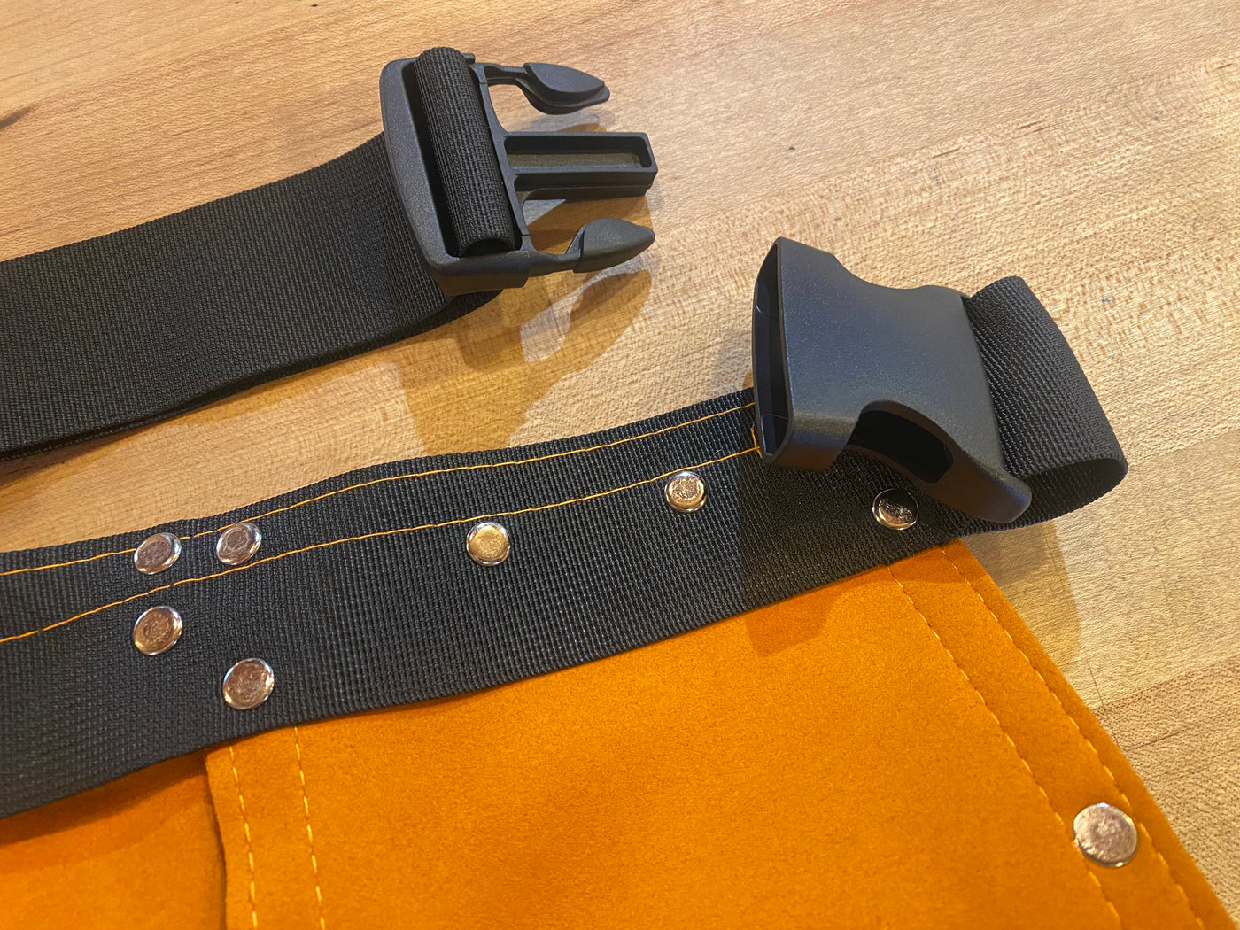 Close-up of Kids Leather Tool Belt by AMZ, featuring an orange fabric design, black adjustable strap, and plastic buckle similar to a microfiber synthetic leather apron, resting on a wooden surface.