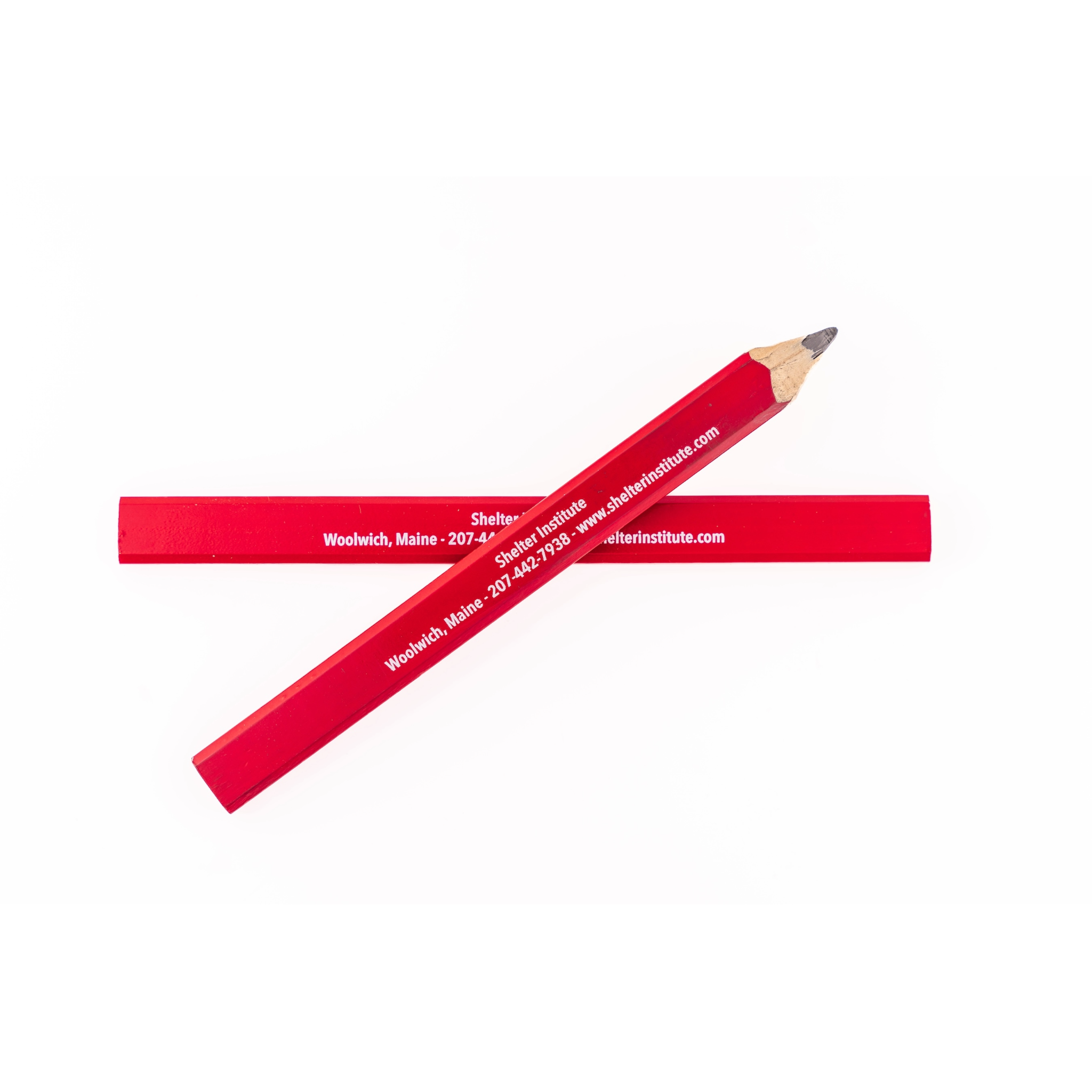 Two Shelter Institute red Carpenter Pencils form an X shape. One reads: "Shelter Institute, Woolwich, Maine 207-442-7938, shelterinstitute.com.