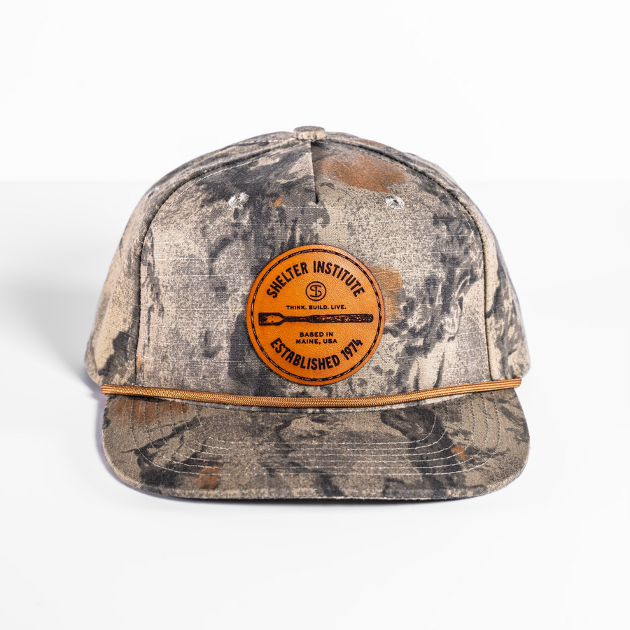 The Shelter Institute Camo Hat, adorned with a bold logo, combines style and function with its sleek camouflage pattern, making it ideal for any adventure.