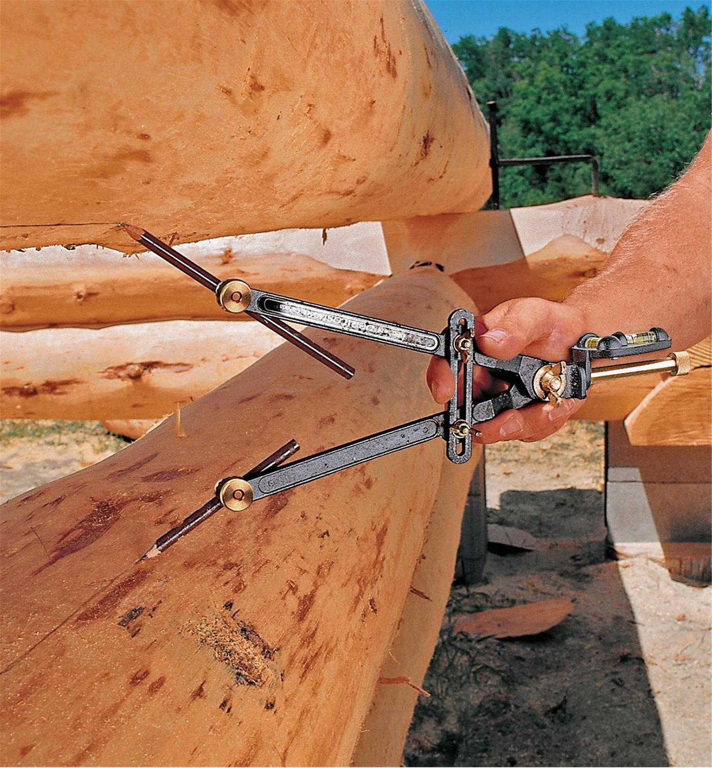 A hand skillfully uses the VER Veritas Transfer/Log Scribe to mark logs at a construction site, set against a backdrop of trees.