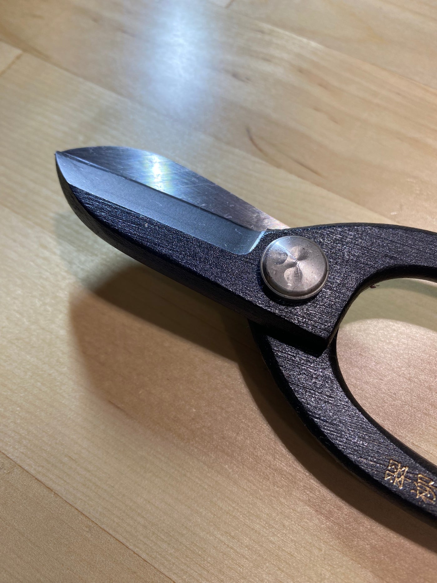 Close-up of MARU Ikebana Shears, crafted from black carbon steel with sharp blades, resting gracefully on a wooden surface.