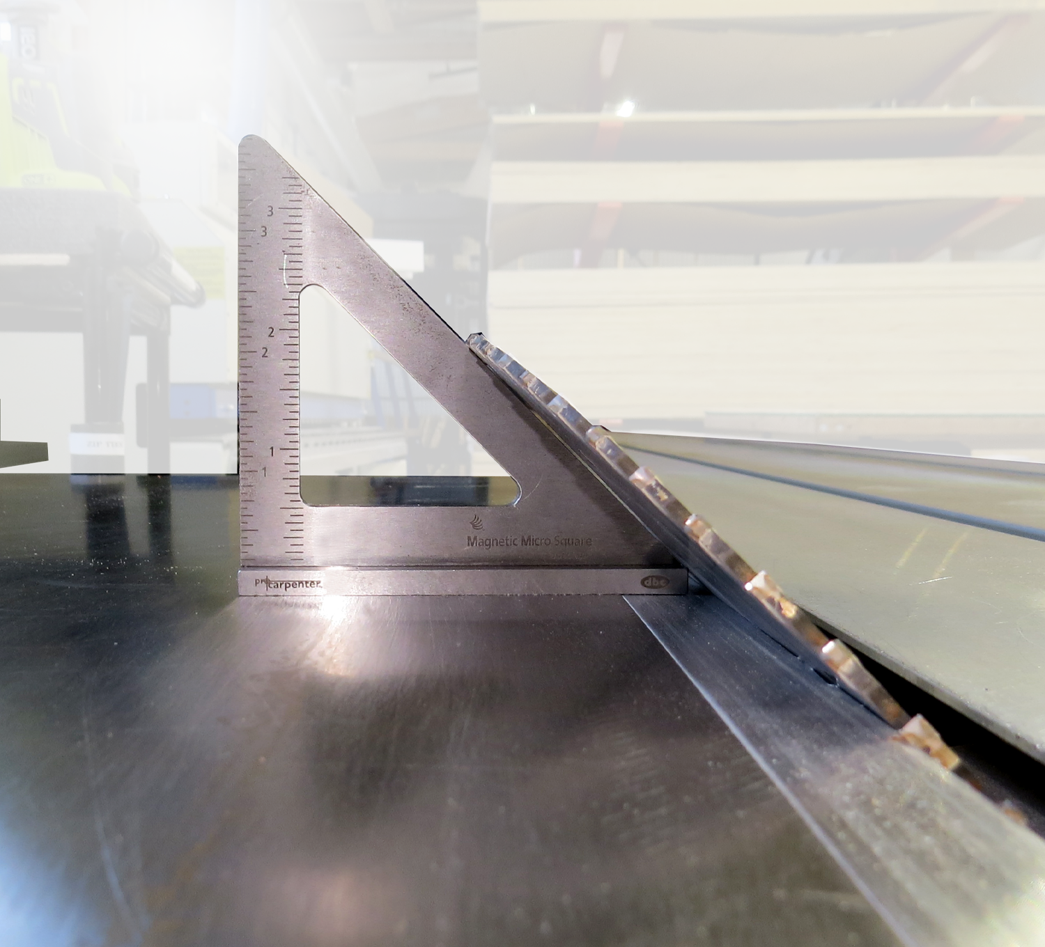 An FTP MAG MICRO SQUARE ruler sits beside a circular saw blade on the workbench, providing precise layout assistance. In the blurred background, stacks of wood emphasize the workshop's organized chaos.