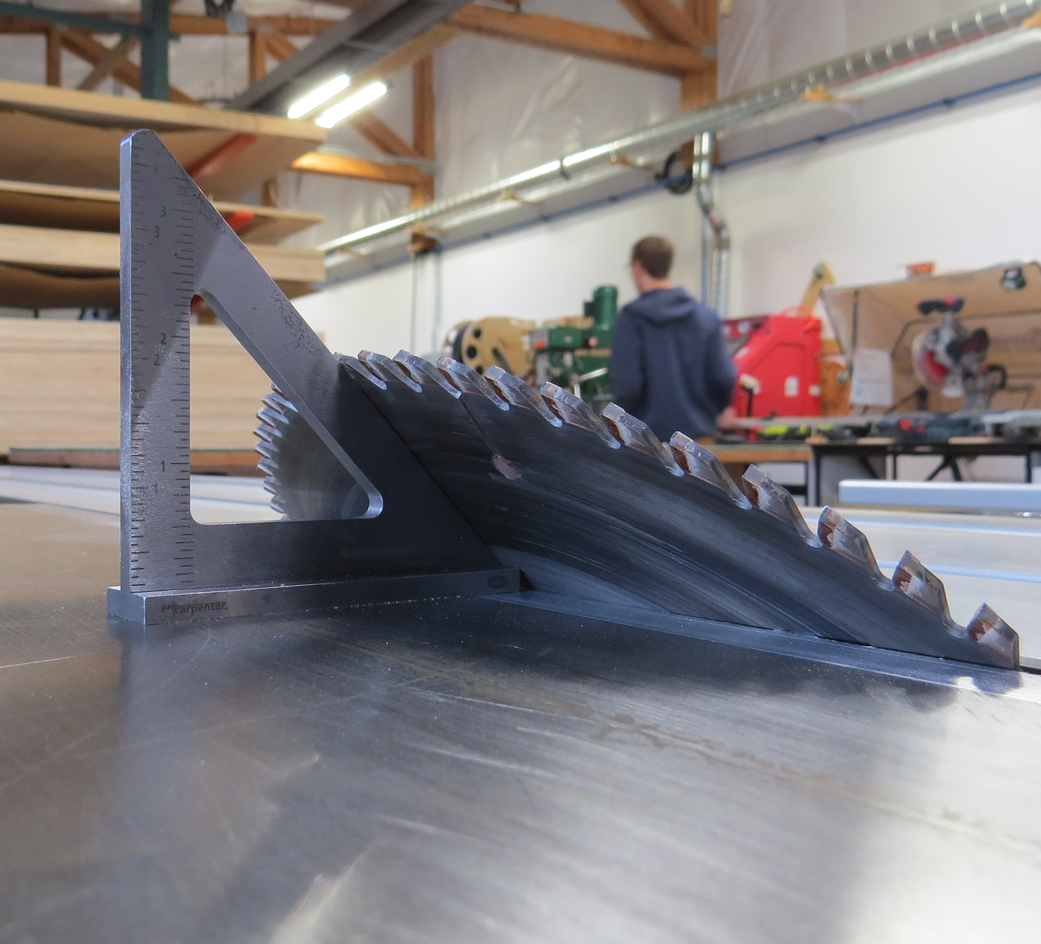 Close-up of a circular saw blade on a table with an FTP MAG MICRO SQUARE and precision layout tool. In the blurred background, someone ensures perfect alignment for each cut.