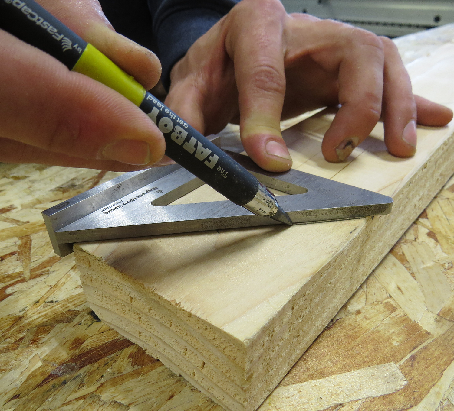 Hands using an FTP MAG MICRO SQUARE and a pencil to mark a precise line on a wooden plank, ensuring an accurate layout with the metallic square.